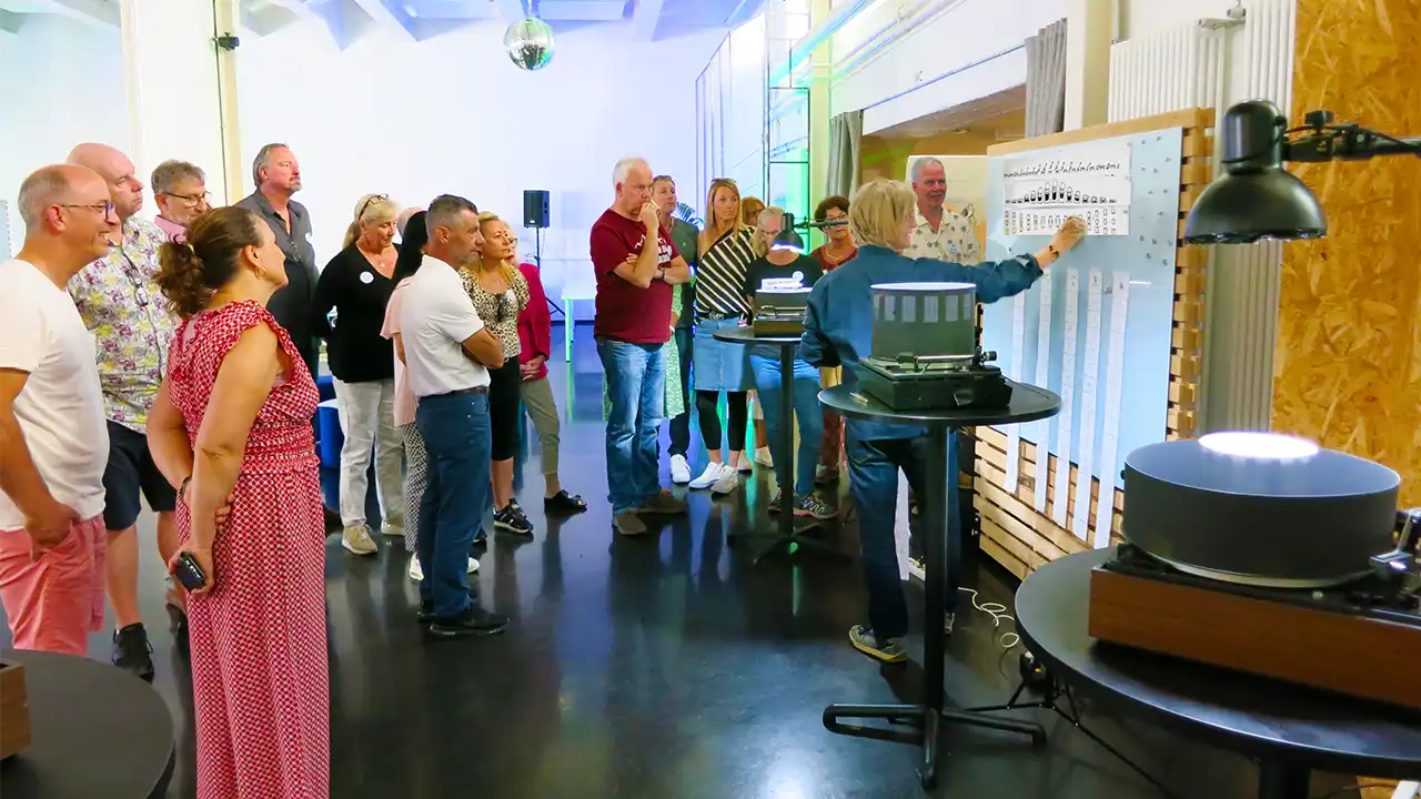 Thomas Stellmach stands in front of a pin board and explains the construction of an animation strip for a zoetrope to the employees of Medland.